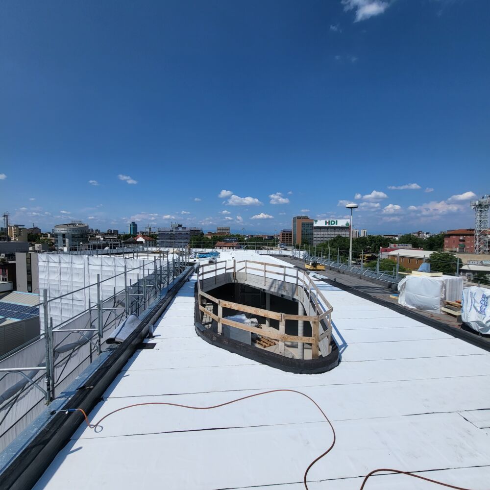 Cantiere M.R. Coperture: tetto piano con membrana bianca, apertura ovale recintata in legno, insegna HDI sullo sfondo